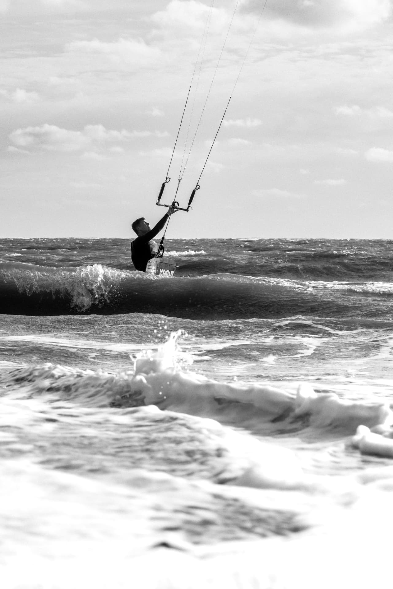 Kitesurfer leaning back against the kite in foamy surf, black and white
