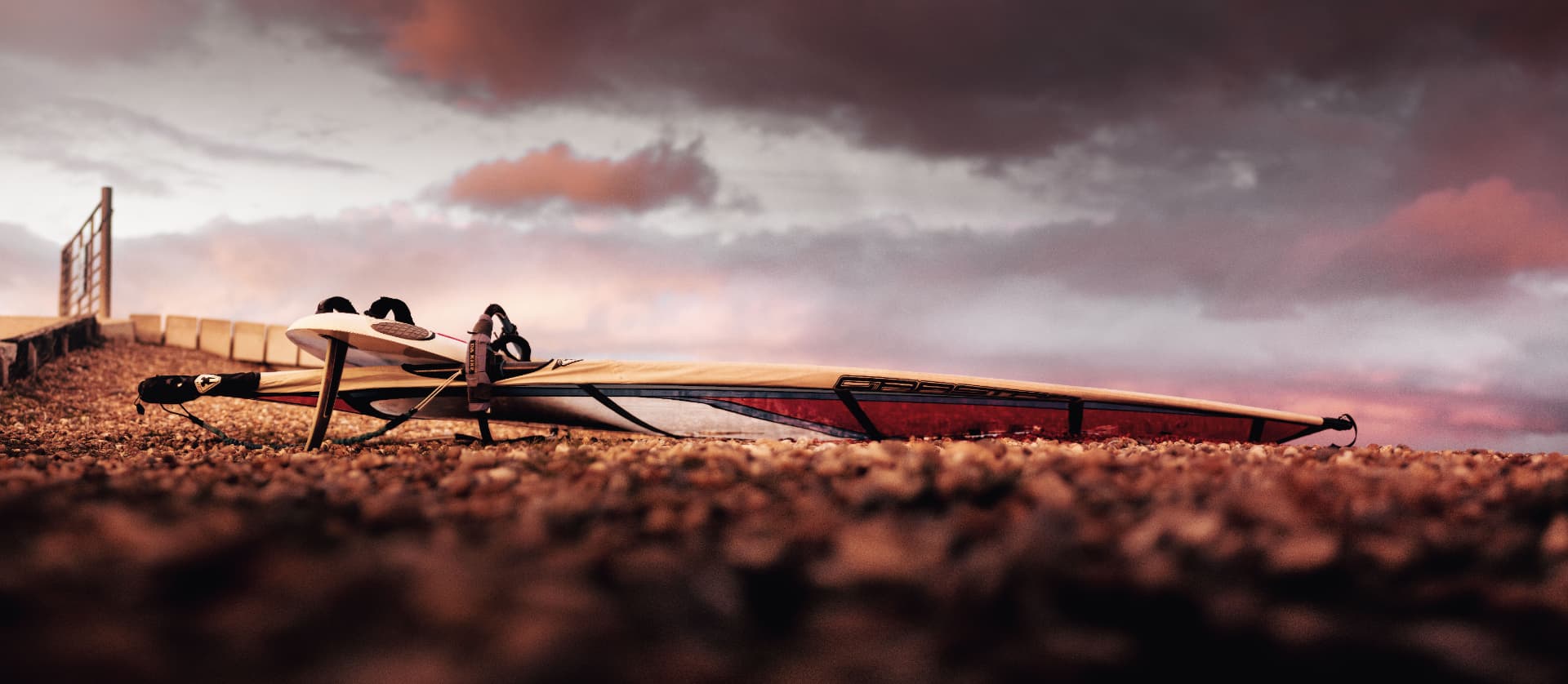 A rigged windsurf board on the shingle under a sunset sky